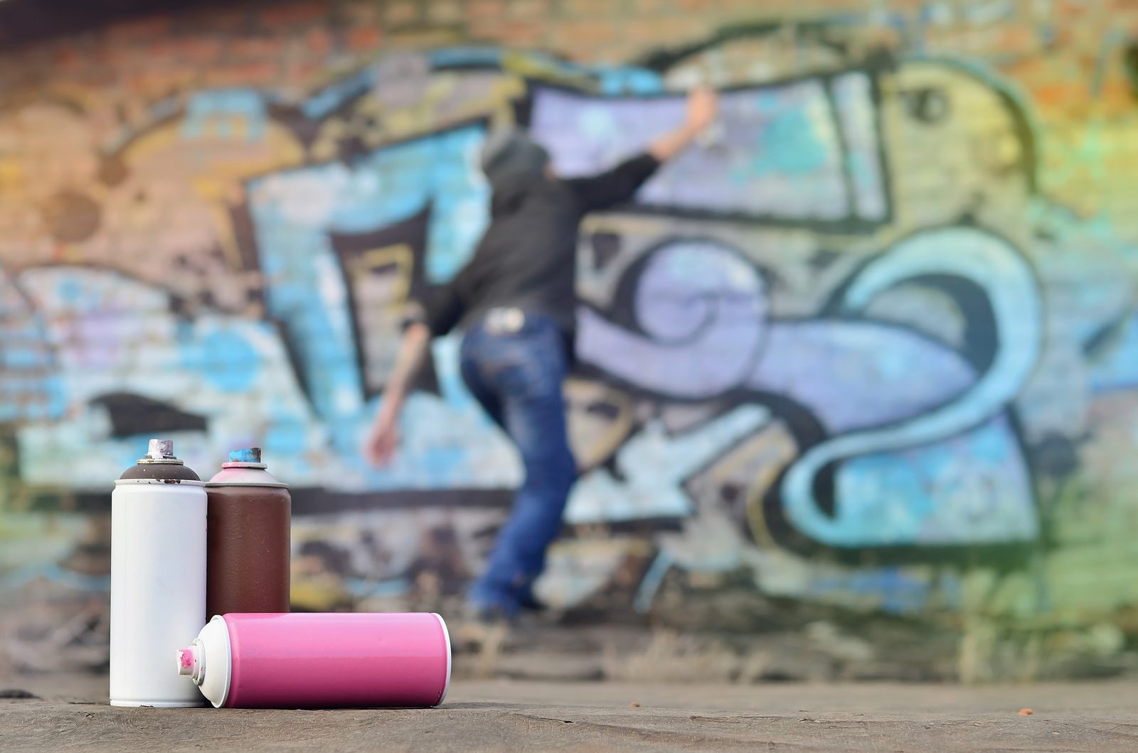 Spray paint cans on the ground near a graffiti-covered wall